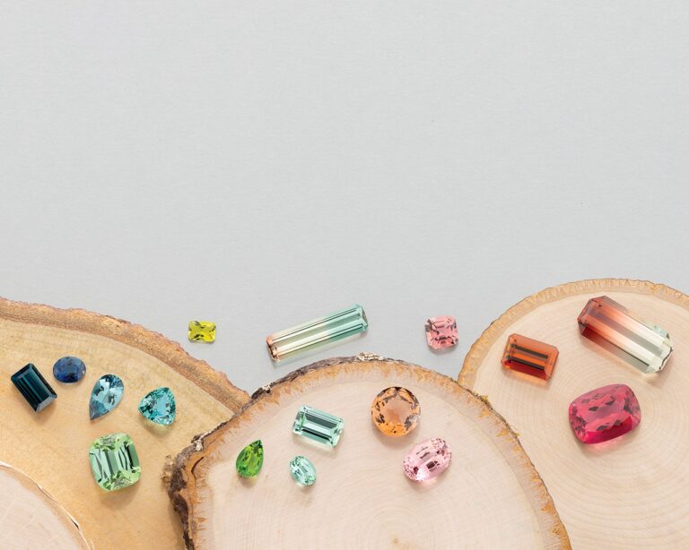 Colorful gemstones including emerald, aquamarine, and topaz arranged on wooden slices, showcasing the beauty and variety of fine jewelry materials.